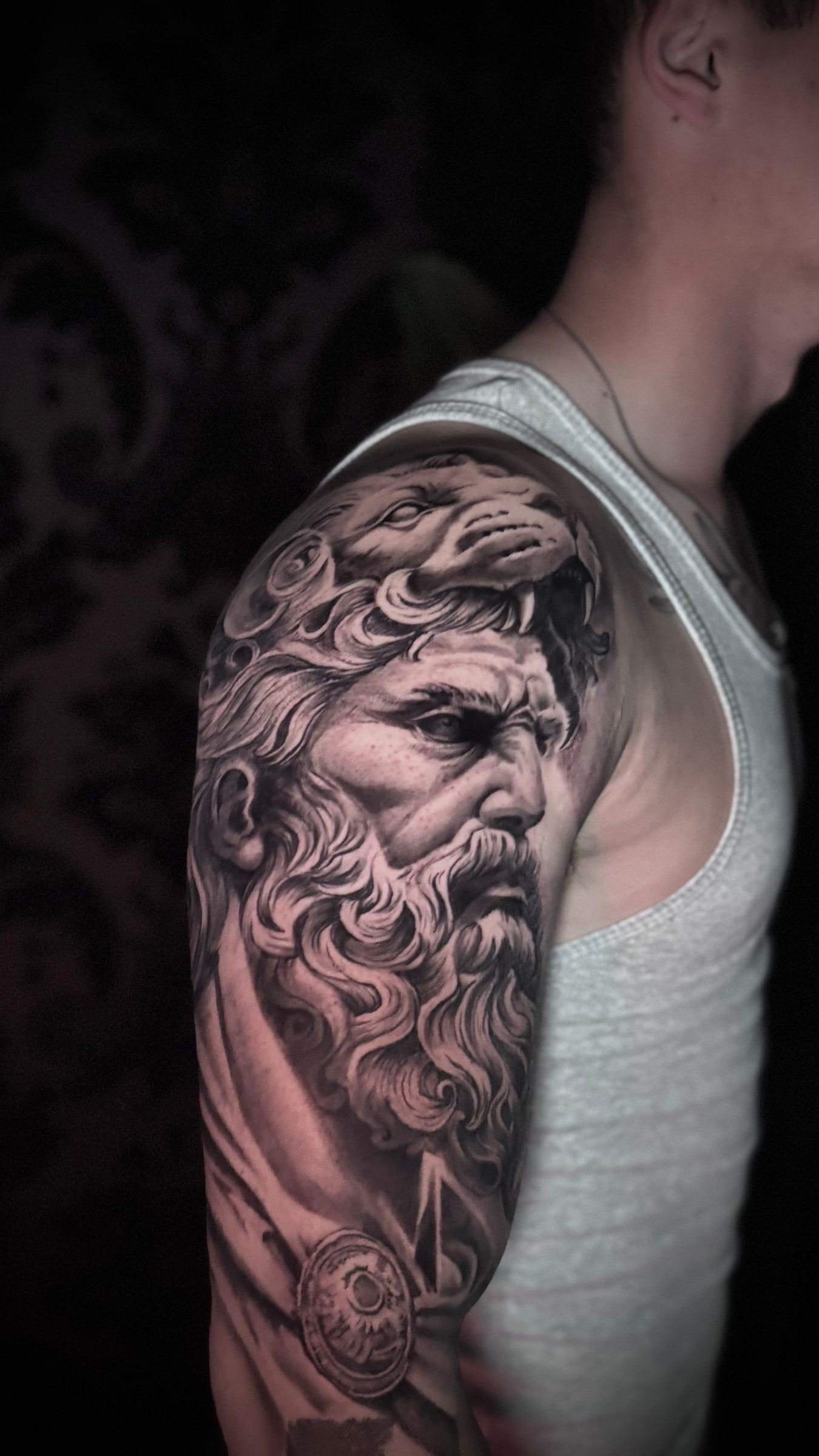 Black and grey realism tattoo of a bearded classical bust with an eagle above it, on an upper arm.