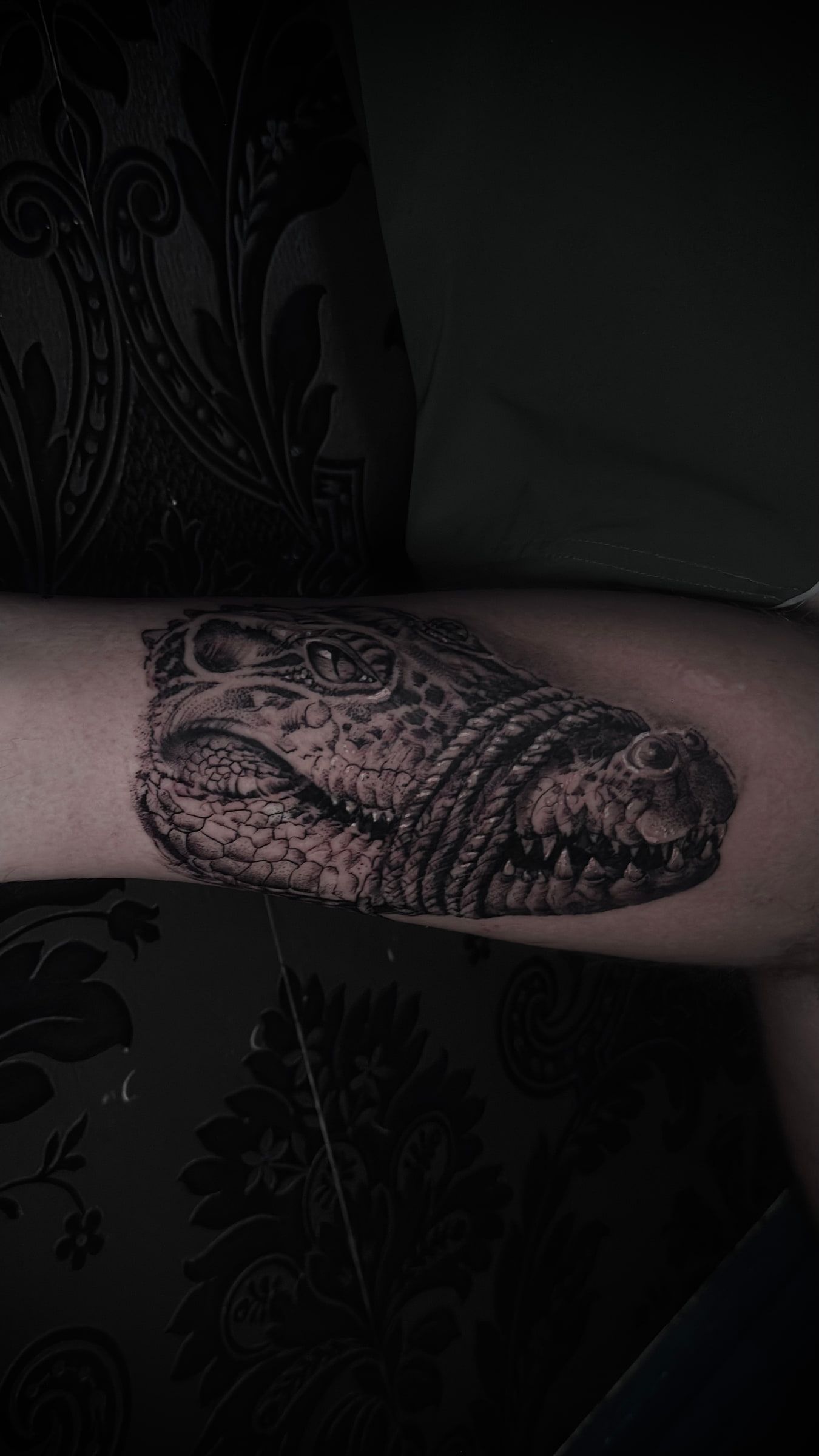 Black and grey realism tattoo of a crocodile's head on a forearm.