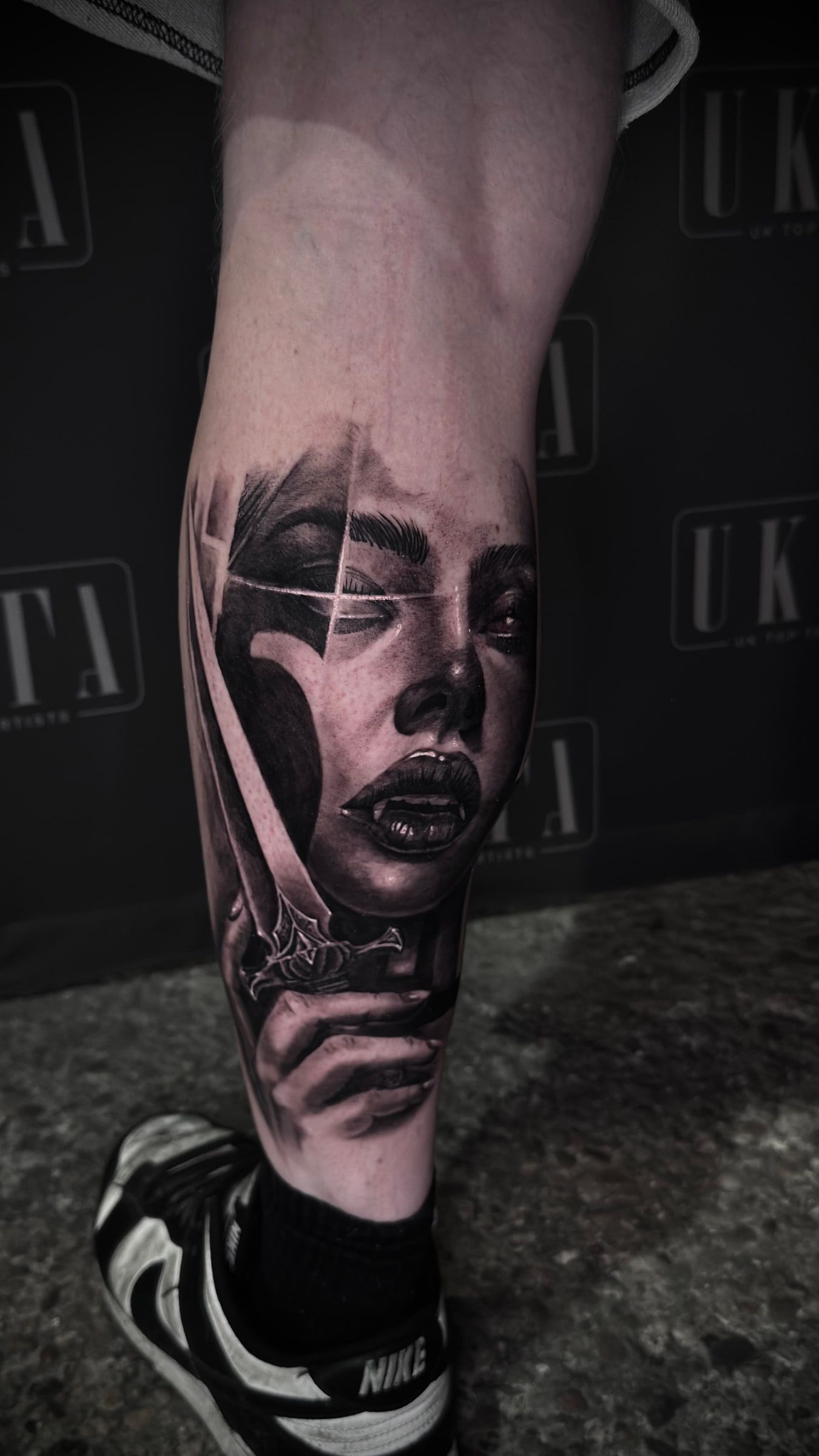 Black and grey realism portrait tattoo of a woman's face, part of it breaking into faceted planes, on a calf.